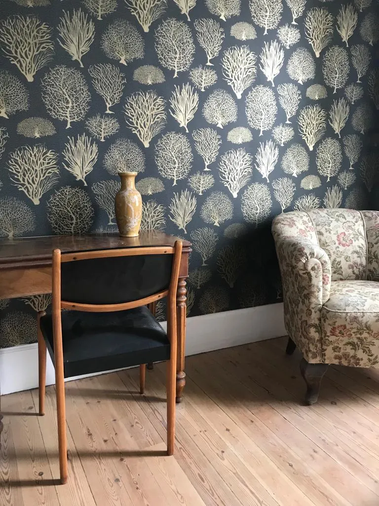 Chambre au papier peint sombre avec fauteuils et vue sur la rue