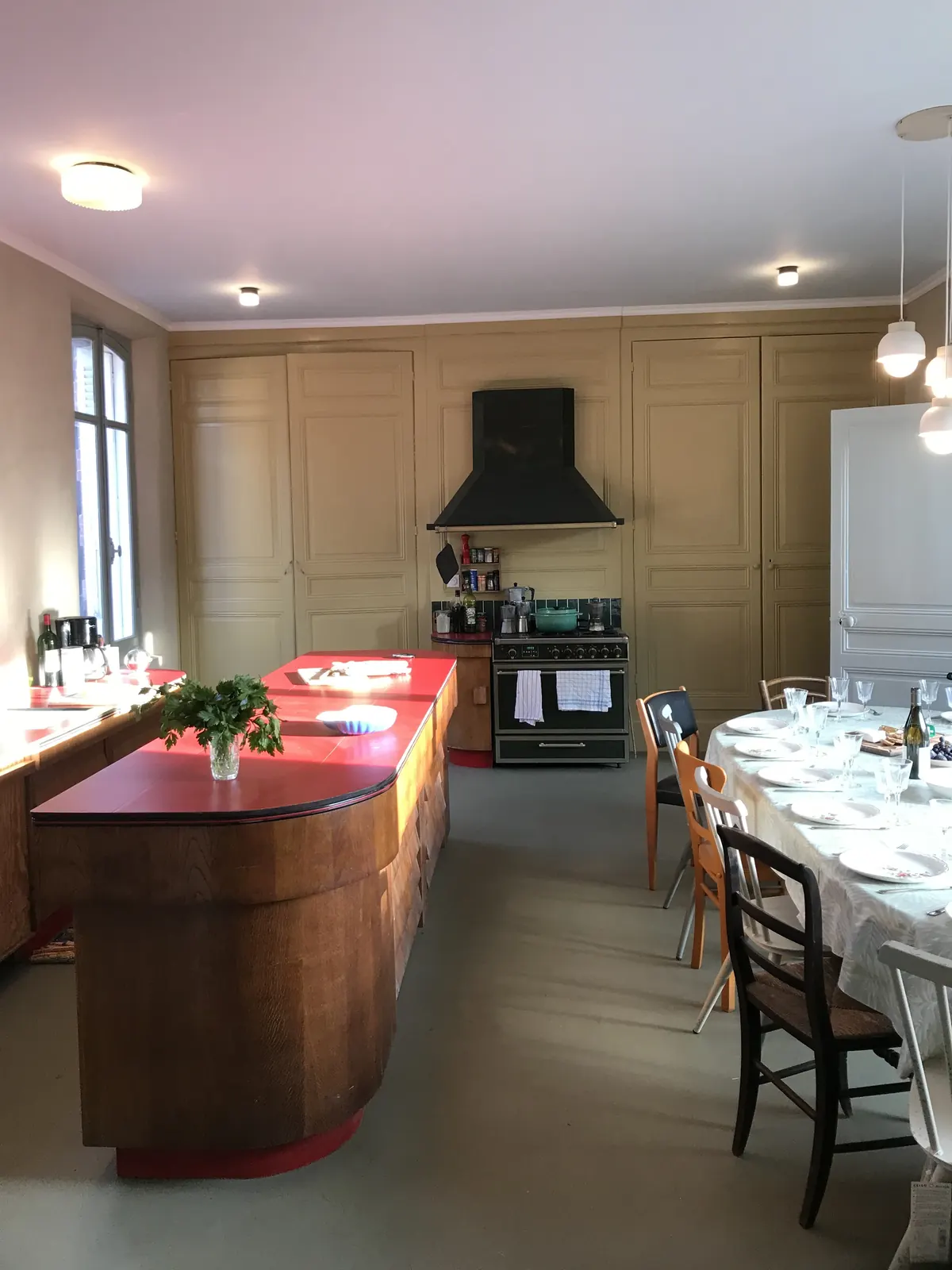 Grande cuisine conviviale : longue tablée dressée, îlot rouge et piano de cuisson