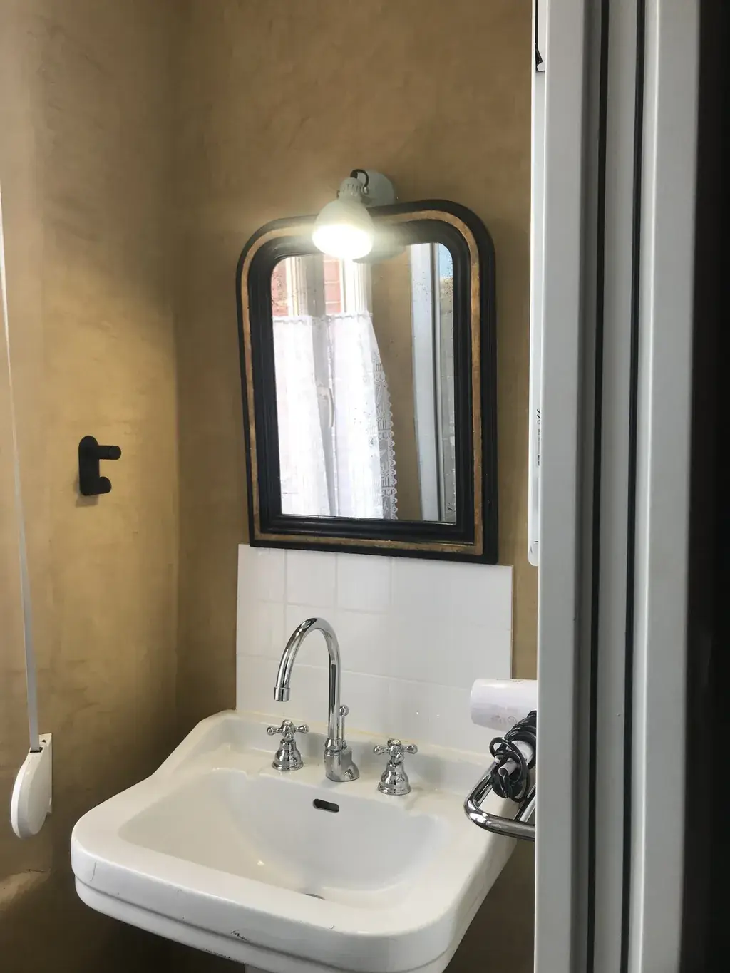 Salle d'eau aux murs ocre avec miroir ancien et robinetterie rétro